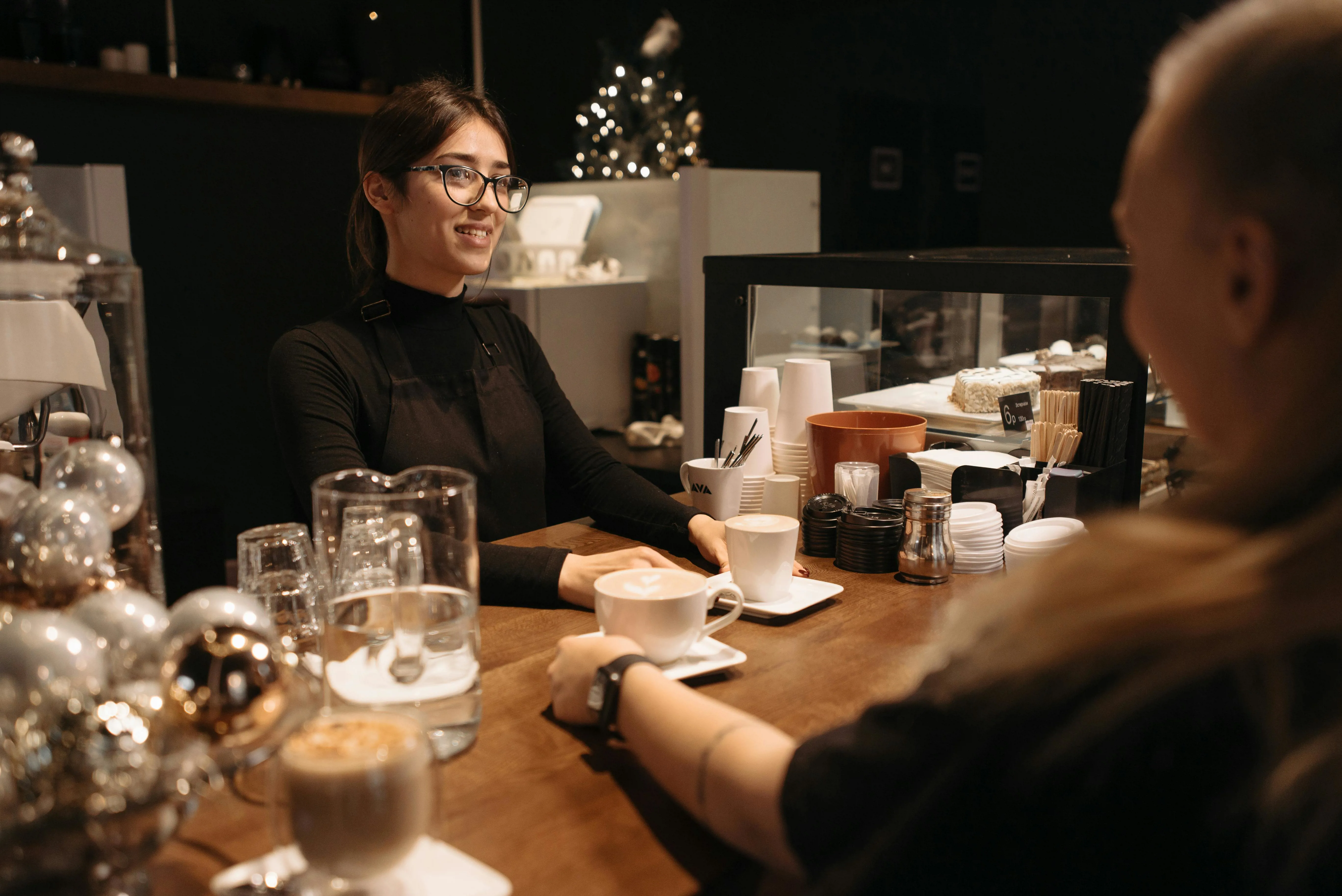 A Woman in Black long Sleeves and Apron Serving Coffee