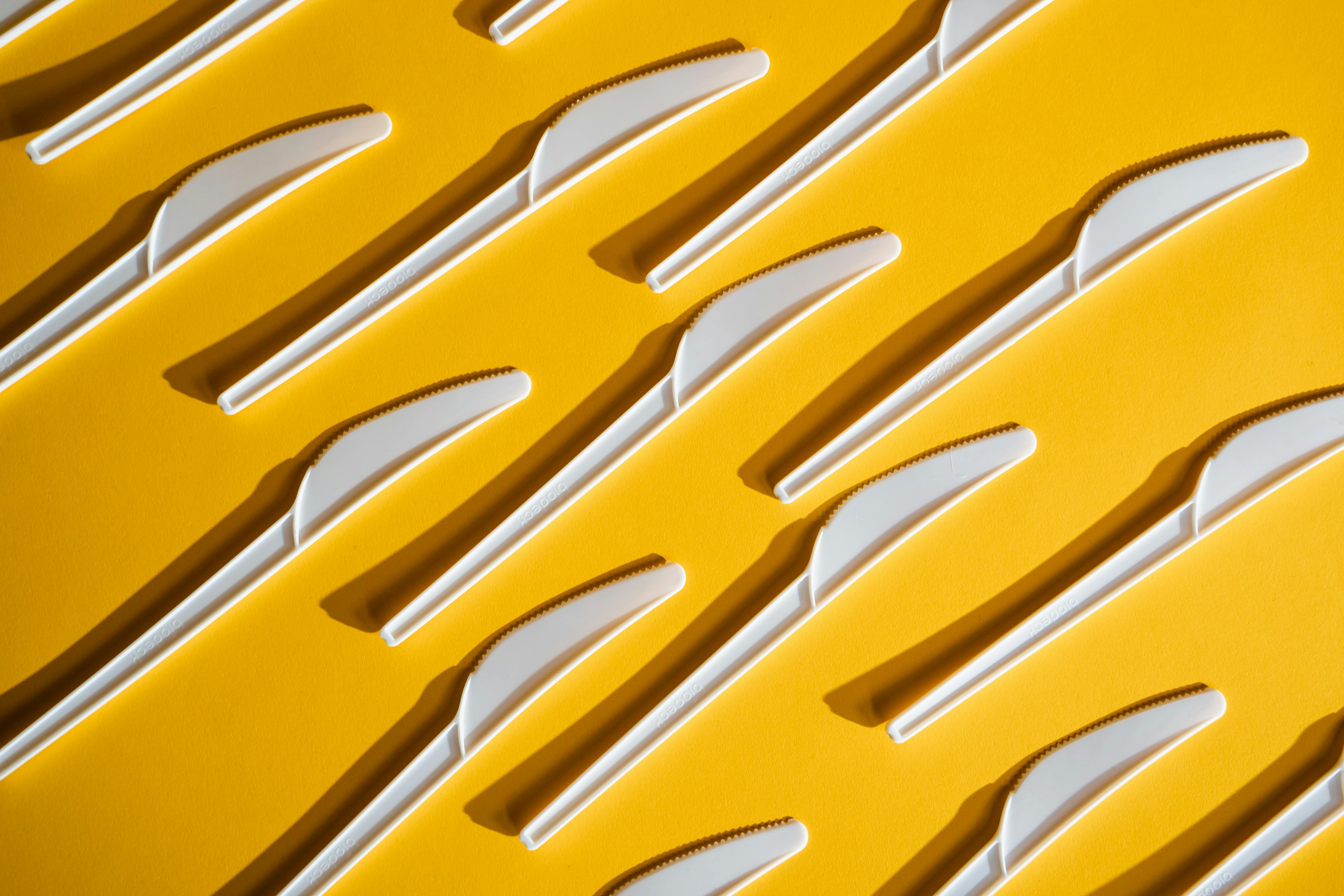 Single-use plastic knives arranged on a yellow background